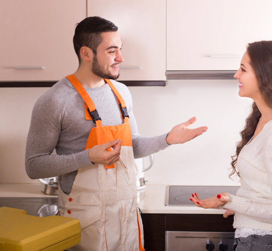 a male plumber talking to a woman about plumbing services in her kitchen
