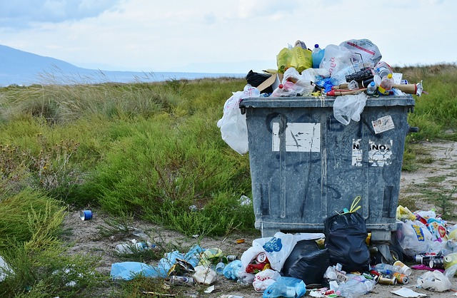 a container of trash in the middle of a filed with trash spilling out onto the ground around it