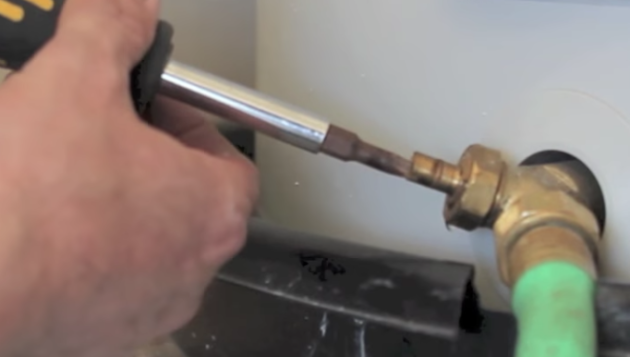 hand using a tool to adjust a part on a water heater