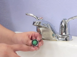 a pair of hands cleaning the aerator of a bathroom sink