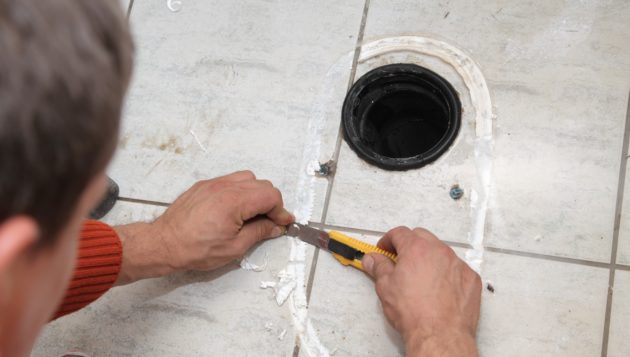 plumber in The Dominion scraping residue off of a tile floor