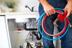 a Hollywood Park plumber holding tools and system parts near a kitchen sink