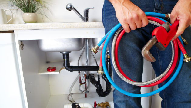 a Hollywood Park plumber holding tools and system parts near a kitchen sink