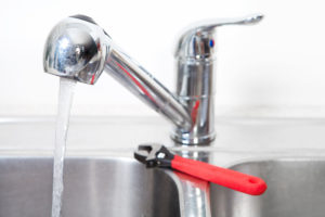 a kitchen sink running with hot water and a wrench on the side of the sink