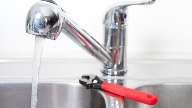 a kitchen sink running with hot water and a wrench on the side of the sink