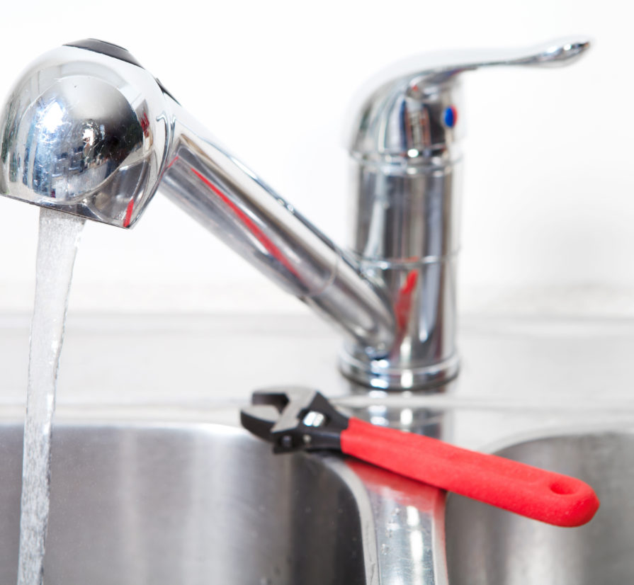 a kitchen sink running with hot water and a wrench on the side of the sink