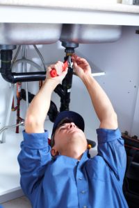 a Windcrest plumber laying down and reaching upwards to adjust the pipes for a kitchen sink.