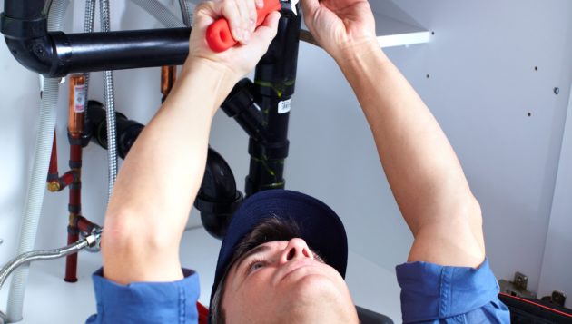 a Windcrest plumber laying down and reaching upwards to adjust the pipes for a kitchen sink.