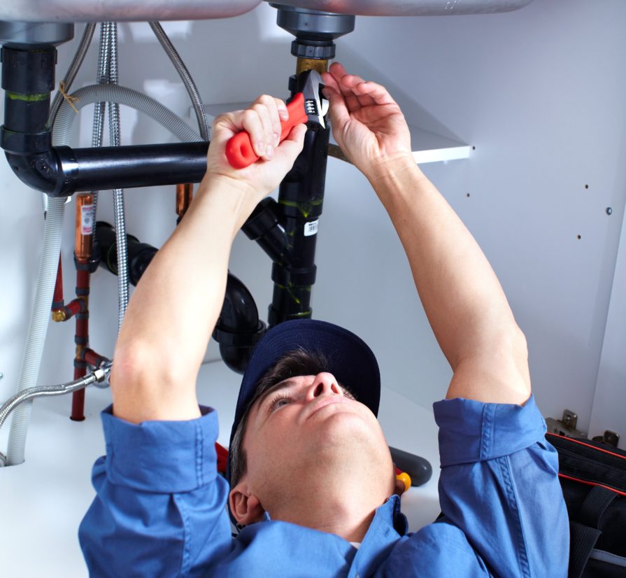 a Windcrest plumber laying down and reaching upwards to adjust the pipes for a kitchen sink.