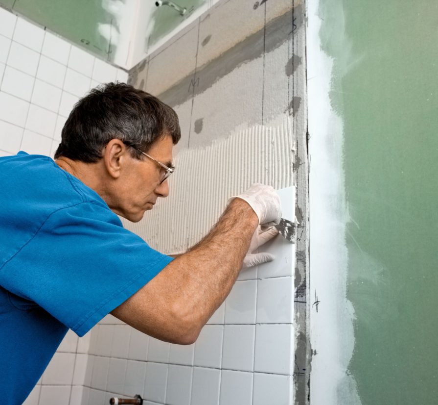 a man performing professional bathroom remodel services for the wall of a shower