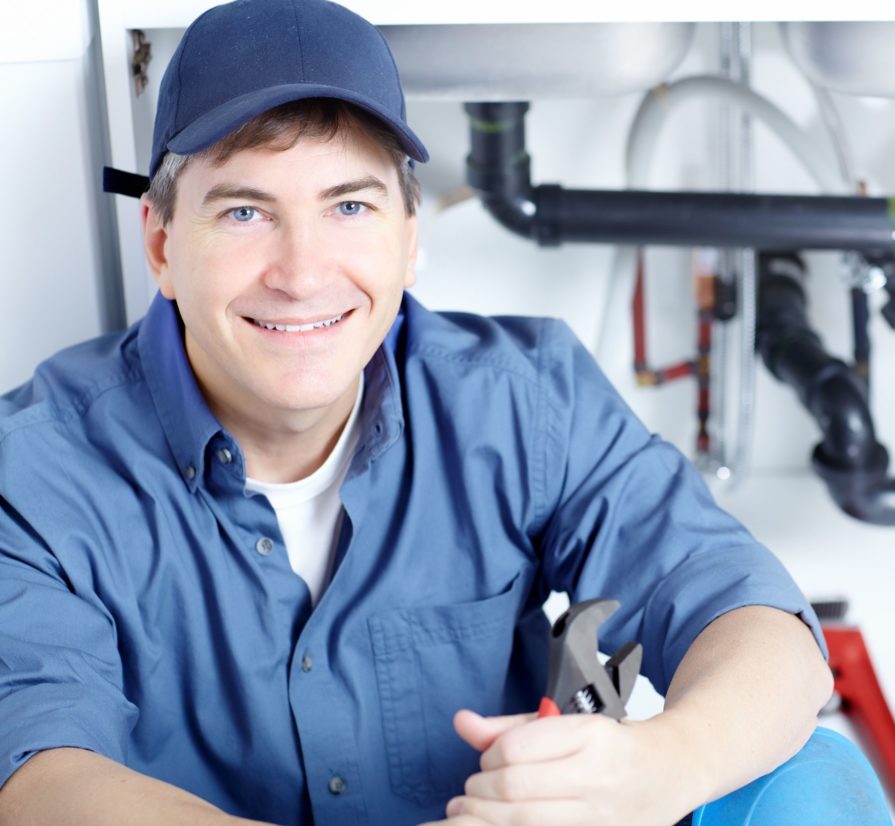 a plumber smiling and holding a wrench in front of pipes