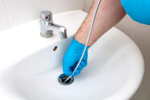 plumber providing drain clearing services while using a drain snake on a bathroom sink