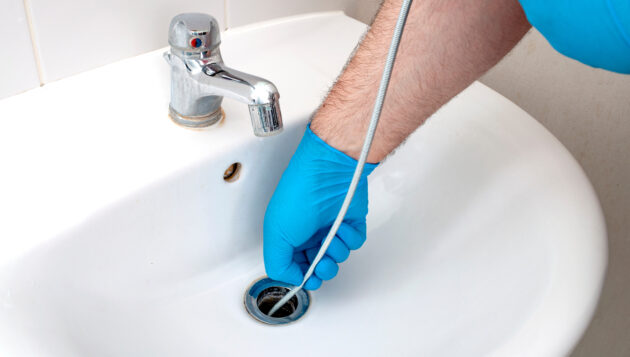 plumber providing drain clearing services while using a drain snake on a bathroom sink