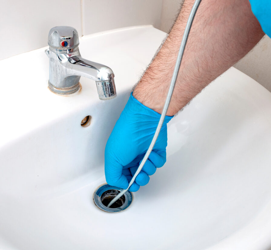 plumber providing drain clearing services while using a drain snake on a bathroom sink