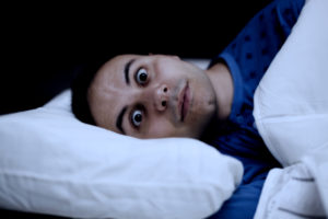 man with wide eyes laying down sideways in bed