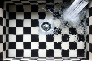 water filling a black and white plaid sink due to a clogged drain