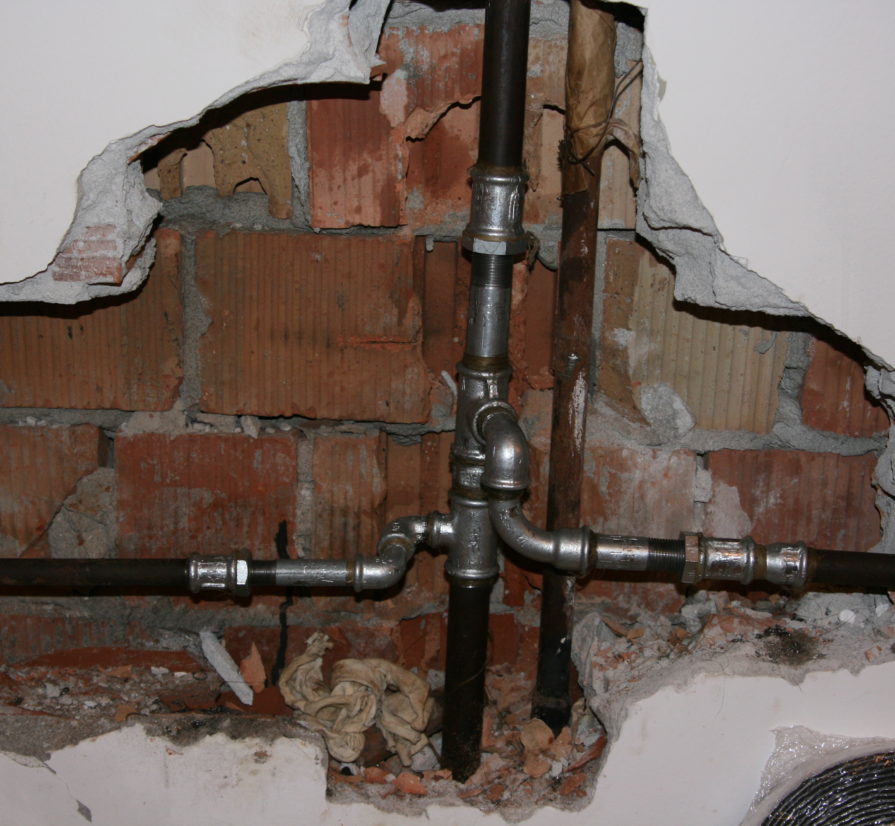 exposed residential plumbing pipes behind a damaged wall