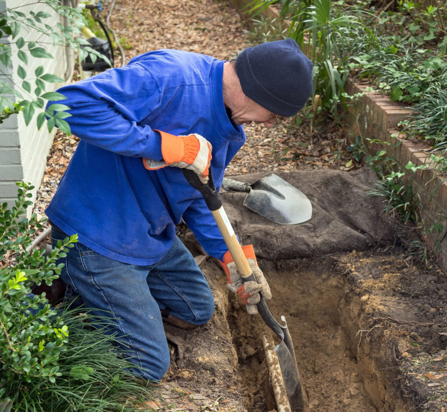 man using a shovel to get access to a collapsed pipe