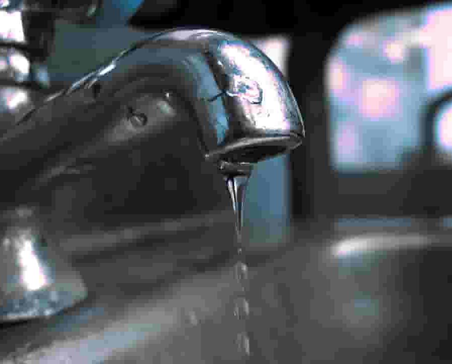 A leaky faucet at a metal sink with water dripping out