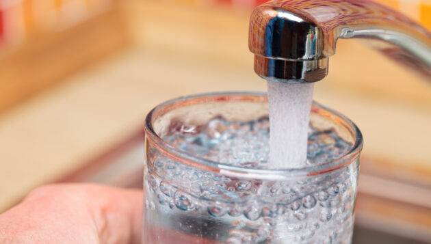 person filling up a glass of water at a kitchen sink faucet