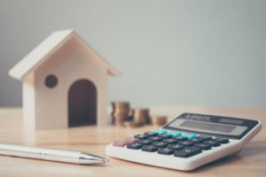 a calculator on a desk with a miniature home model and coins