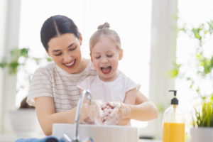 a mother helping her daughter wash her hands at a sink