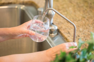 hands filling up a glass of water from a kitchen sink