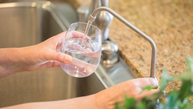 hands filling up a glass of water from a kitchen sink