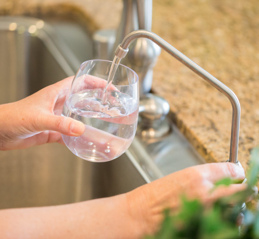 hands filling up a glass of water from a kitchen sink