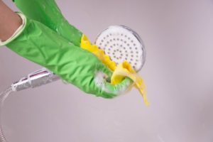 gloved hands using soapy water to clean a showerhead