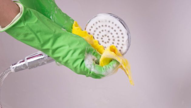 gloved hands using soapy water to clean a showerhead