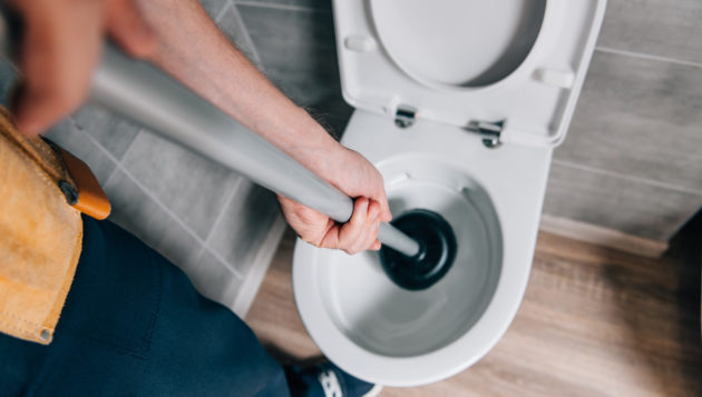 a plumber using a plunger on a toilet