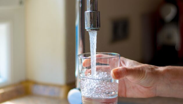 a woman's hand filling up a glass of water from a kitchen sink